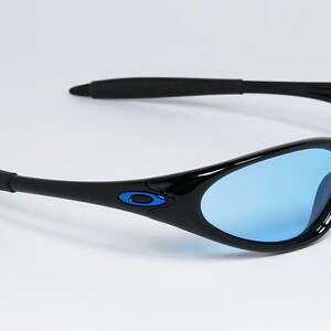 May include: Black sunglasses with blue lenses. The sunglasses have a sleek, curved design with black frames and temples. A small blue accent is visible on the frame near the temple. The lenses are a light blue color.