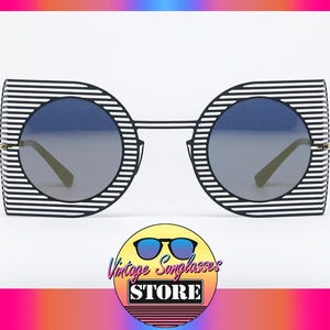 Könnte beinhalten: Schwarz-weiße gestreifte Sonnenbrille mit runden Gläsern. Die Sonnenbrille hat einen goldenen Metallrahmen.