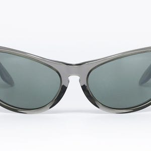 May include: Gray sunglasses with a curved frame and dark lenses. The Ray-Ban logo is visible on the left lens. The sunglasses have a sleek, modern design, suitable for outdoor activities.