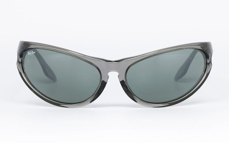 May include: Gray sunglasses with a curved frame and dark lenses. The Ray-Ban logo is visible on the left lens. The sunglasses have a sleek, modern design, suitable for outdoor activities.