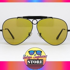 Puede incluir: Gafas de sol estilo aviador con lentes amarillas y montura negra. Las gafas tienen doble puente y barra superior curvada. El logotipo de Vintage Sunglasses Store est&aacute; en la parte inferior de la imagen.