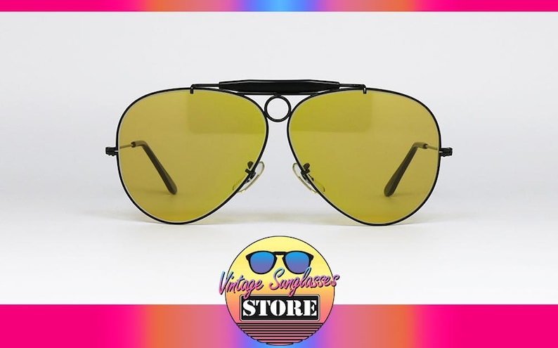 Puede incluir: Gafas de sol estilo aviador con lentes amarillas y montura negra. Las gafas tienen doble puente y barra superior curvada. El logotipo de Vintage Sunglasses Store est&aacute; en la parte inferior de la imagen.