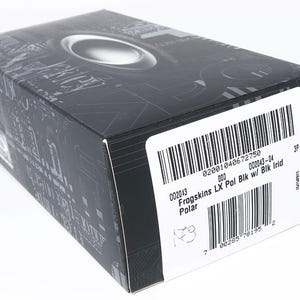 May include: Black box with a silver oval design on the top. The box has a barcode and text that reads "Frogskins LX Pol Bik w/ Blk Irid Polar". The box is on a white background.