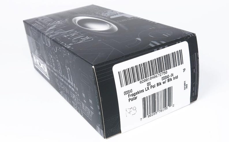 May include: Black box with a silver oval design on the top. The box has a barcode and text that reads "Frogskins LX Pol Bik w/ Blk Irid Polar". The box is on a white background.