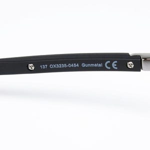 May include: Close-up of a portion of eyeglasses. The frame is black with a red accent and the text "137 OX3235-0454 Gunmetal CE" is printed on the arm. The hinge is silver.