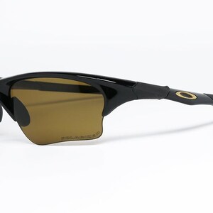 May include: Black sunglasses with brown tinted lenses. The sunglasses have a sleek, curved design with a gold-colored logo on the temple. The lenses are polarized.