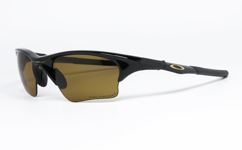 May include: Black sunglasses with brown tinted lenses. The sunglasses have a sleek, curved design with a gold-colored logo on the temple. The lenses are polarized.