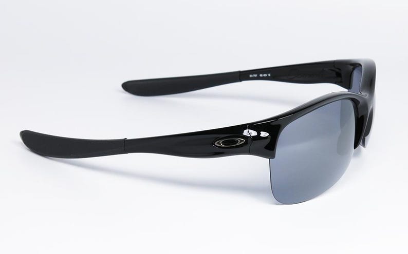 May include: Black sunglasses with gray lenses. The sunglasses have a glossy finish and a curved design. The arms of the sunglasses are thick and have a slight curve. The lenses are a gray color and are partially rimless.