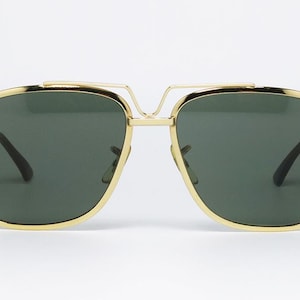 Puede incluir: Gafas de sol con montura dorada y lentes verde oscuro. Las gafas tienen un doble puente y forma rectangular. Las monturas son de color dorado brillante y las lentes son de color verde oscuro s&oacute;lido. Las gafas son de estilo aviador cl&aacute;sico.