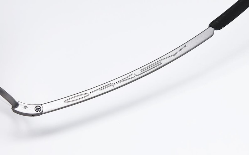May include: A close-up of the silver metal arm of a pair of sunglasses with the word "Oakley" engraved on it.