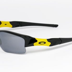 K&ouml;nnte beinhalten: Schwarze und gelbe Sportsonnenbrille mit grauen Gl&auml;sern. Die Sonnenbrille hat ein schlankes, modernes Design mit einem schwarzen Rahmen und gelben Akzenten an den B&uuml;geln. Die Gl&auml;ser sind dunkelgrau und bieten Sonnenschutz.