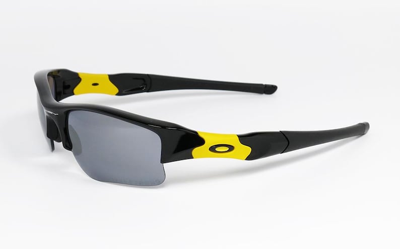 K&ouml;nnte beinhalten: Schwarze und gelbe Sportsonnenbrille mit grauen Gl&auml;sern. Die Sonnenbrille hat ein schlankes, modernes Design mit einem schwarzen Rahmen und gelben Akzenten an den B&uuml;geln. Die Gl&auml;ser sind dunkelgrau und bieten Sonnenschutz.