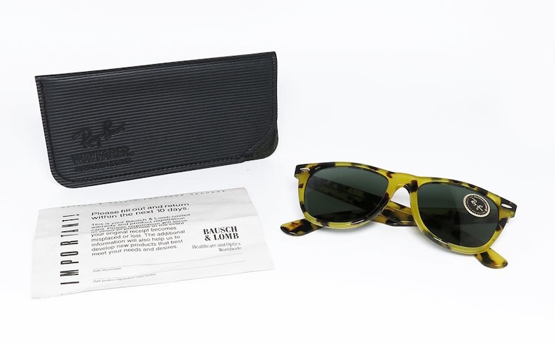 May include: A pair of yellow and black tortoise shell sunglasses with dark lenses, a black leather case, and a white paper with text. The sunglasses have a round logo on the lens.