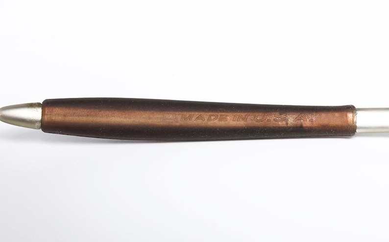 May include: A pen with a silver tip and a brown handle. The handle has the text "MADE IN U.S.A." engraved on it. The pen is set against a white background.