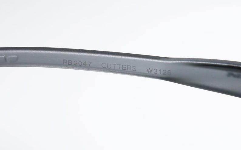 May include: Close-up of a gray eyeglass arm with the text "RB 2047 CUTTERS W3126" printed in white. The arm is curved and appears to be made of plastic or a similar material. The background is plain white.