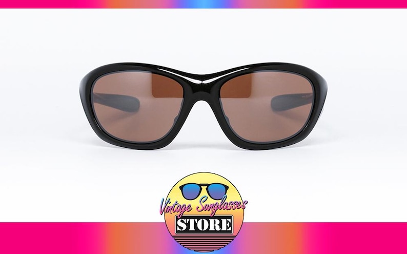 K&ouml;nnte beinhalten: Schwarze Sonnenbrille mit braunen Gl&auml;sern. Die Sonnenbrille hat einen abgerundeten, dicken Rahmen. Das Bild enth&auml;lt ein Logo f&uuml;r einen Vintage-Sonnenbrillenladen.