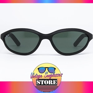 Pode incluir: &Oacute;culos de sol Ray-Ban pretos com arma&ccedil;&atilde;o oval e lentes verde escuro. Os &oacute;culos de sol t&ecirc;m um acabamento fosco e um logotipo Ray-Ban sutil na haste. A imagem est&aacute; em um fundo branco.