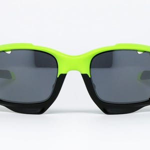 May include: Sport sunglasses with a neon green frame and black accents. The lenses are a dark gray color. The sunglasses have a modern, angular design, suitable for outdoor activities.