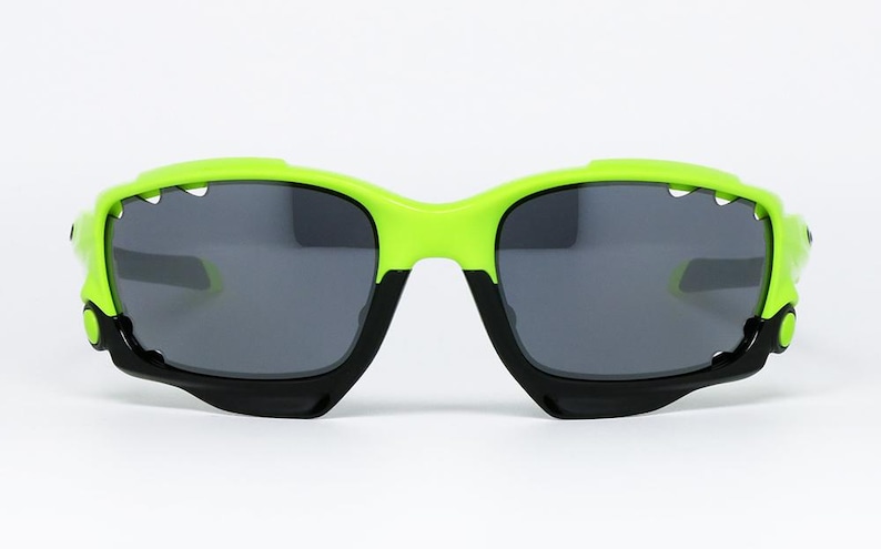 May include: Sport sunglasses with a neon green frame and black accents. The lenses are a dark gray color. The sunglasses have a modern, angular design, suitable for outdoor activities.