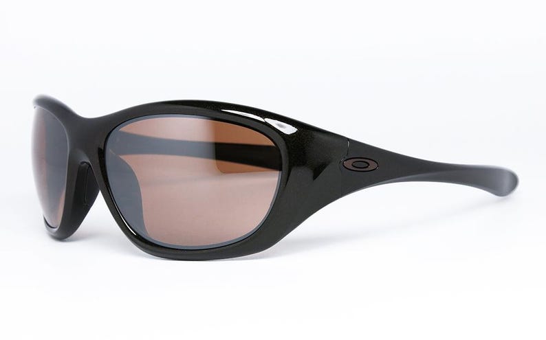K&ouml;nnte beinhalten: Schwarze Sonnenbrille mit braun get&ouml;nten Gl&auml;sern. Die Sonnenbrille hat ein geschwungenes, umlaufendes Design mit gl&auml;nzendem Finish. Das Oakley-Logo ist auf dem B&uuml;gel sichtbar. Diese Sonnenbrille ist f&uuml;r Outdoor-Aktivit&auml;ten konzipiert.