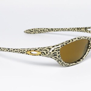 May include: Leopard print sunglasses with brown lenses. The frames feature a tan and black spotted pattern. The Oakley logo is visible on the temples. These sunglasses are a stylish accessory for eye protection.