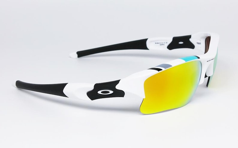 May include: White and black sunglasses with yellow mirrored lenses. The sunglasses have a sporty design with a white frame, black arms, and a black logo on the side. The lenses are a bright yellow color.