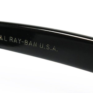 K&ouml;nnte beinhalten: Nahaufnahme des schwarzen Plastikb&uuml;gels einer Sonnenbrille mit der Aufschrift "B&L RAY-BAN U.S.A." in wei&szlig;.