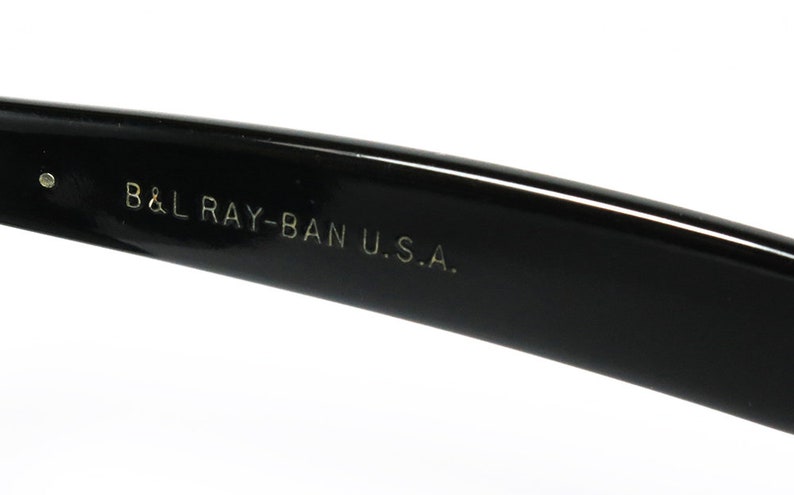 K&ouml;nnte beinhalten: Nahaufnahme des schwarzen Plastikb&uuml;gels einer Sonnenbrille mit der Aufschrift "B&L RAY-BAN U.S.A." in wei&szlig;.