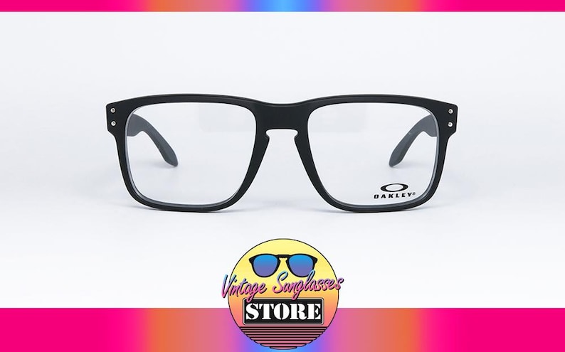 May include: Black Oakley spectacles with a square frame and clear lenses. The Oakley logo is visible on the right lens. The glasses are set against a white background with a colourful gradient at the top and bottom.