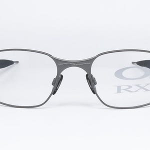 May include: A pair of gray metal eyeglasses with clear lenses. The lenses have the text "Oakley RX" printed on them.
