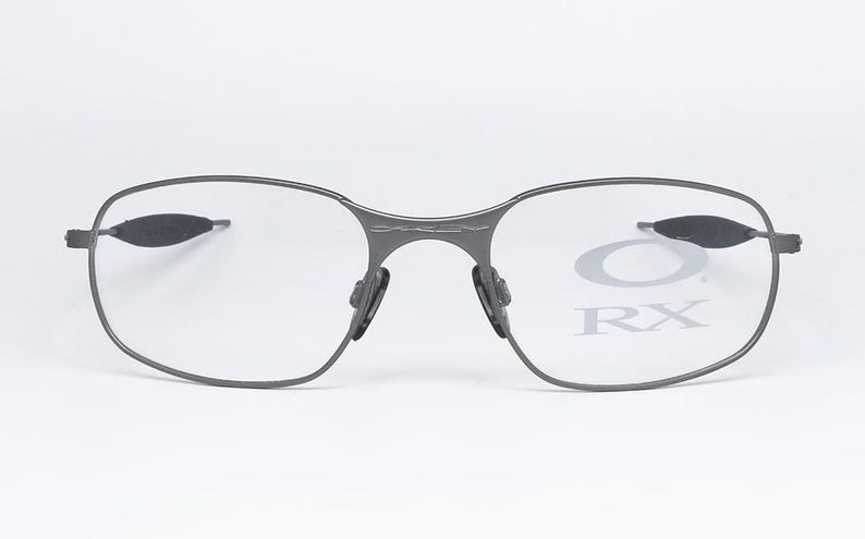 May include: A pair of gray metal eyeglasses with clear lenses. The lenses have the text "Oakley RX" printed on them.