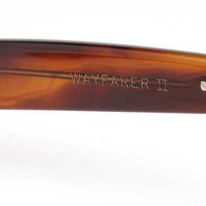 Peut inclure: Gros plan sur la monture en &eacute;caille brune d'une paire de lunettes de soleil Wayfarer II. La monture est dot&eacute;e d'une charni&egrave;re argent&eacute;e et le texte "WAYFARER II" est grav&eacute; sur le c&ocirc;t&eacute;.