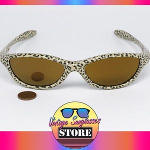 May include: Vintage sunglasses with a leopard print frame and brown lenses. The sunglasses are set against a white background with a coin and a logo that says "Vintage Sunglasses Store".