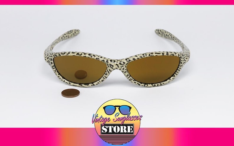 May include: Vintage sunglasses with a leopard print frame and brown lenses. The sunglasses are set against a white background with a coin and a logo that says "Vintage Sunglasses Store".
