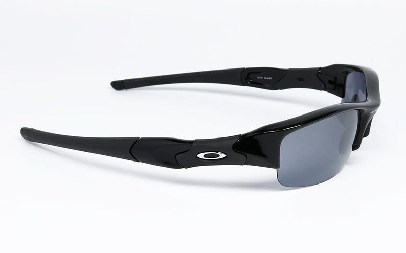K&ouml;nnte beinhalten: Schwarze Sonnenbrille mit grauen Gl&auml;sern. Die Sonnenbrille hat einen gl&auml;nzend schwarzen Rahmen und ein silbernes Logo an den B&uuml;geln. Die B&uuml;gel sind gebogen und erstrecken sich nach au&szlig;en. Die Gl&auml;ser sind dunkelgrau.
