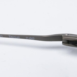 May include: Close-up of the arm of a pair of glasses. The arm is made of titanium and has the numbers 130, 11-643 printed on it.