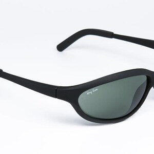 Pode incluir: &Oacute;culos de sol pretos com arma&ccedil;&atilde;o curva e lentes cinzentas. O log&oacute;tipo Ray-Ban &eacute; vis&iacute;vel na lente. Os &oacute;culos de sol t&ecirc;m um design desportivo e s&atilde;o adequados para atividades ao ar livre.