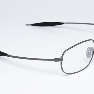May include: A pair of silver-toned metal eyeglasses with clear lenses. The glasses have a thin, wire frame and black rubber earpieces.