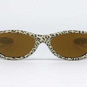 May include: Sunglasses with a leopard print pattern on the frames. The lenses are a warm brown color. The sunglasses are set against a white background.