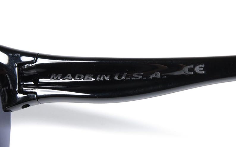 May include: Close-up of a black sunglasses arm. The text "MADE IN U.S.A." is embossed on the arm. The letters "CE" are also visible. The sunglasses appear to be made of a glossy material.