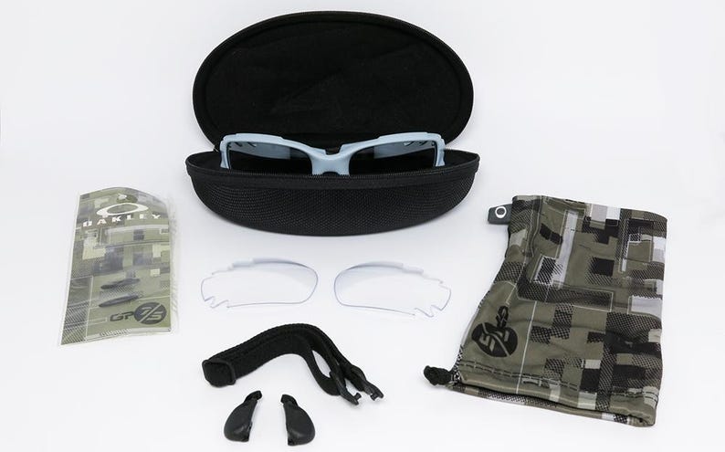 May include: A light blue sports sunglasses set with a black case, extra lenses, and accessories. The set includes a camouflage-patterned pouch and a clear lens set. The sunglasses are in a black case.