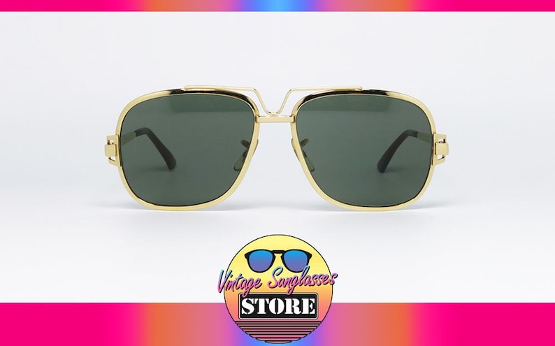 Puede incluir: Gafas de sol doradas con lentes verde oscuro. Las gafas tienen forma cuadrada con doble puente y patillas negras. La imagen incluye un logotipo de Vintage Sunglasses Store.