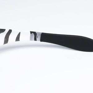 May include: Sunglasses with a black and white zebra print pattern on the arms. The earpiece is black, and the frame is a dark color. The sunglasses are set against a white background.