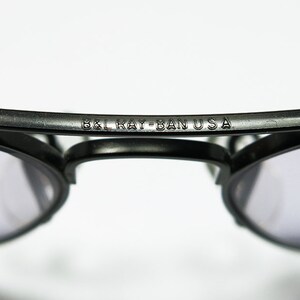 May include: Close-up of a pair of black sunglasses with the text "B&L Ray-Ban USA" engraved on the frame.