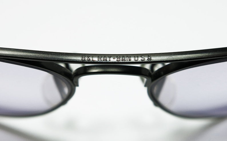 May include: Close-up of a pair of black sunglasses with the text "B&L Ray-Ban USA" engraved on the frame.