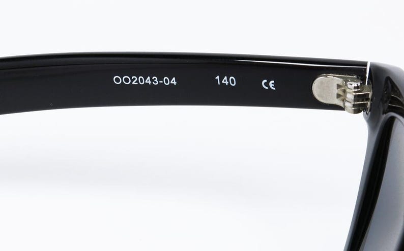 May include: Close-up of the arm of black eyeglasses. The text "OO2043-04" and "140" are printed in white. The hinge is silver. The frame is glossy.