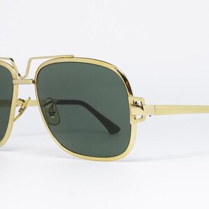Puede incluir: Gafas de sol de aviador con montura dorada y lentes verde oscuro. Las gafas tienen un doble puente y un dise&ntilde;o elegante. Las patillas son doradas con puntas marrones oscuras. Un accesorio elegante.