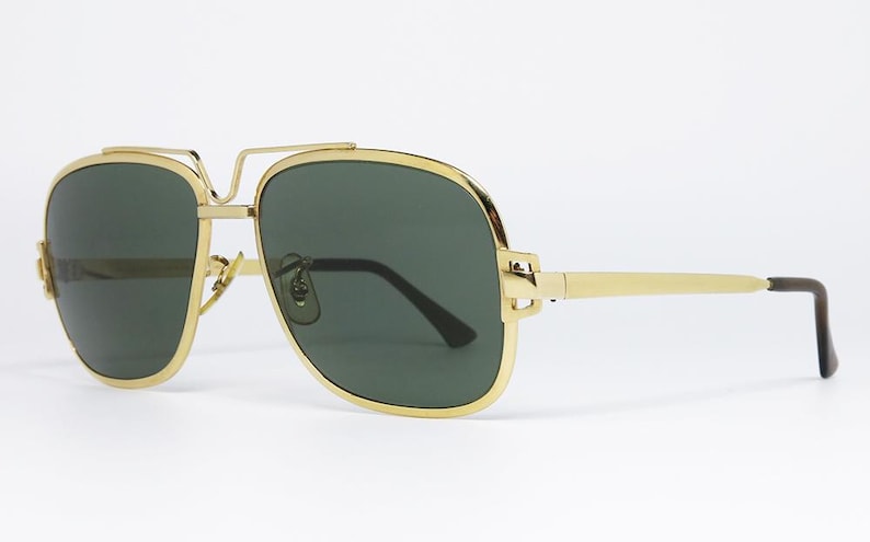 Puede incluir: Gafas de sol de aviador con montura dorada y lentes verde oscuro. Las gafas tienen un doble puente y un dise&ntilde;o elegante. Las patillas son doradas con puntas marrones oscuras. Un accesorio elegante.
