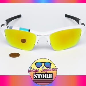 May include: White and black sunglasses with yellow lenses. The sunglasses have a white frame and black arms. A penny is next to the sunglasses. The image also includes a logo that says "Vintage Sunglasses Store".