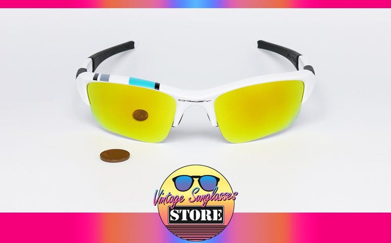 May include: White and black sunglasses with yellow lenses. The sunglasses have a white frame and black arms. A penny is next to the sunglasses. The image also includes a logo that says "Vintage Sunglasses Store".